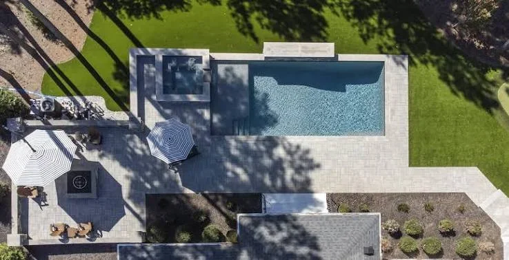 Aerial view of rectangular pool with concrete patio, lounge area, and manicured lawn
