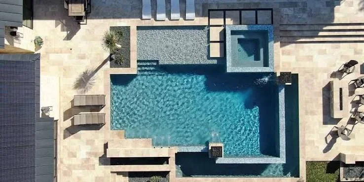 Aerial view of geometric swimming pool with spa, travertine decking, and lounge areas