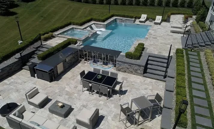Large in-ground pool with spa, paver patio, outdoor kitchen, and fire pit surrounded by landscaping