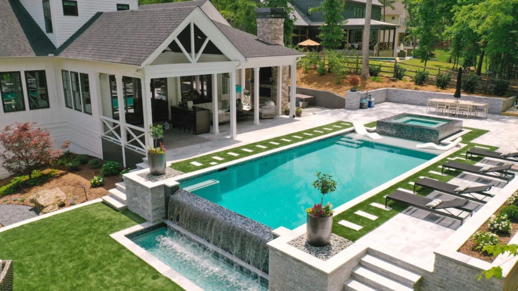 Infinity pool with spa, stone waterfall, composite deck, and poolhouse with X-pattern railings