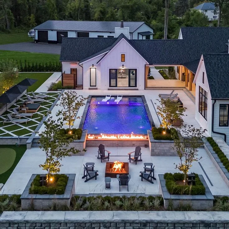 Lit swimming pool with LED lighting, fire feature, and paver patio in modern backyard design