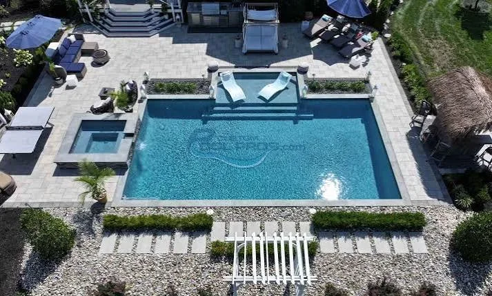 Aerial view of rectangular pool with gray paver deck, spa, and lounge seating