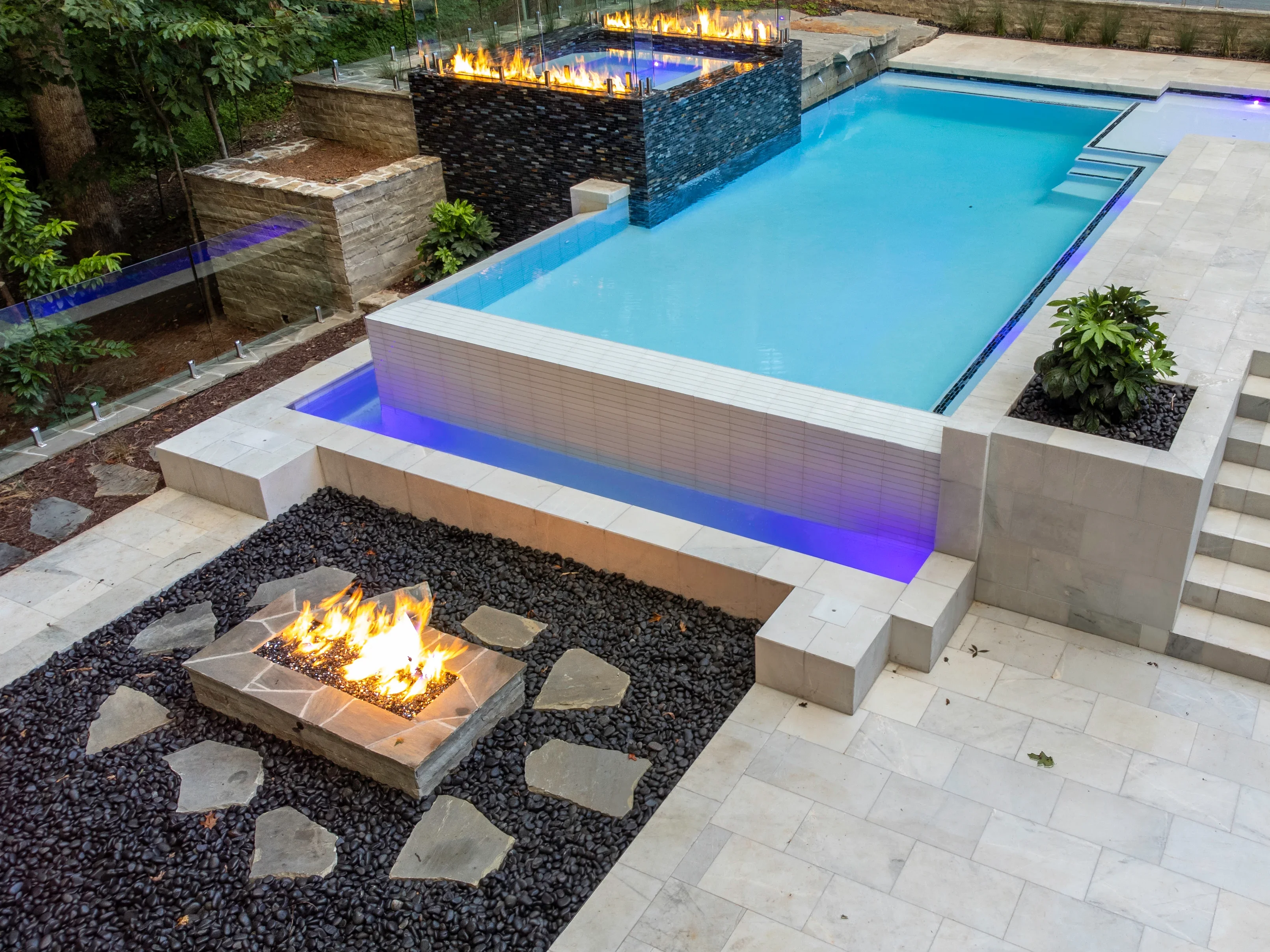 Turquoise pool with LED lighting, sunken fire pit, black river rock, concrete decking and spa