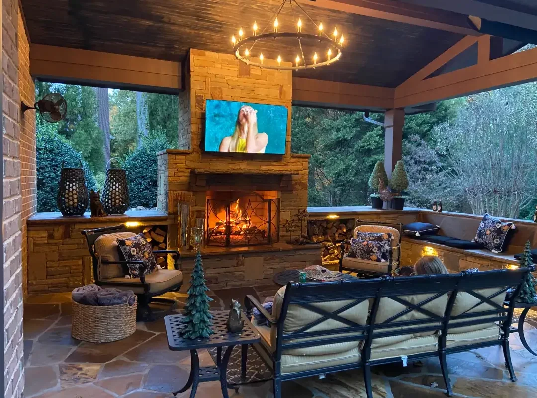 Stone fireplace with TV mount, circular chandelier, built-in seating, and concrete patio under covered structure