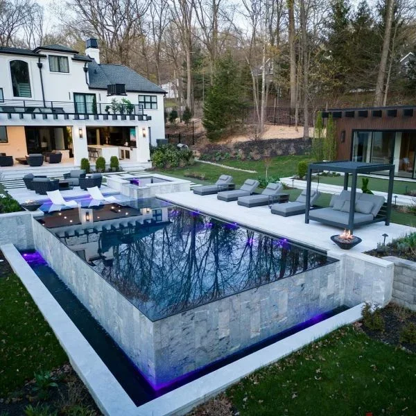 Geometric concrete pool with purple LED lighting, spa, and expansive deck with lounge seating