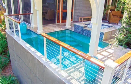 Residential pool with turquoise water, concrete deck, stainless steel cable railings, and white columns