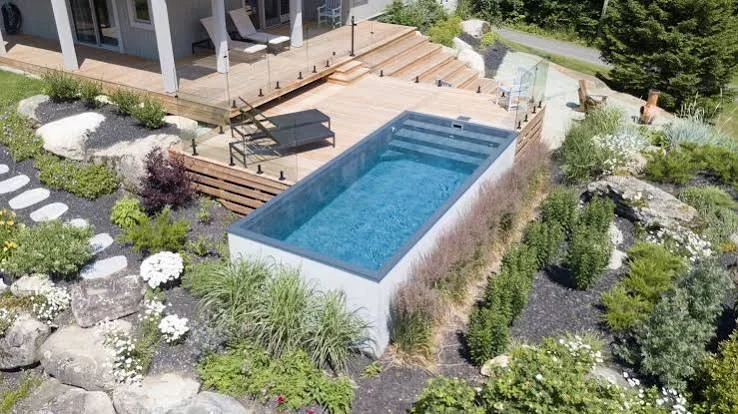 Rectangular swimming pool with blue finish, wooden deck, metal railings, and landscaped surroundings