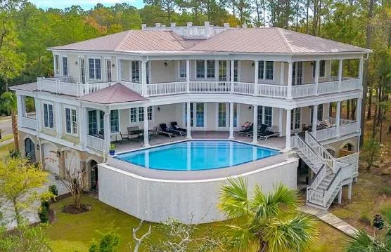 Curved swimming pool with blue interior, concrete deck, and wraparound design behind two-story home
