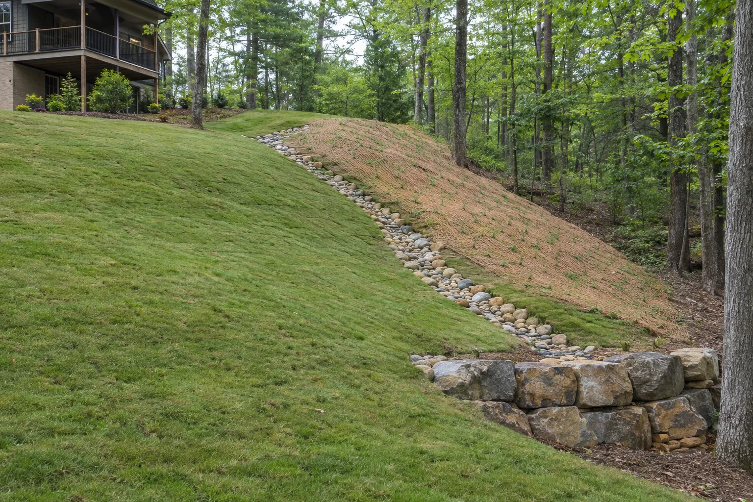 Regraded backyard slope with new sod and a rock-lined swale
