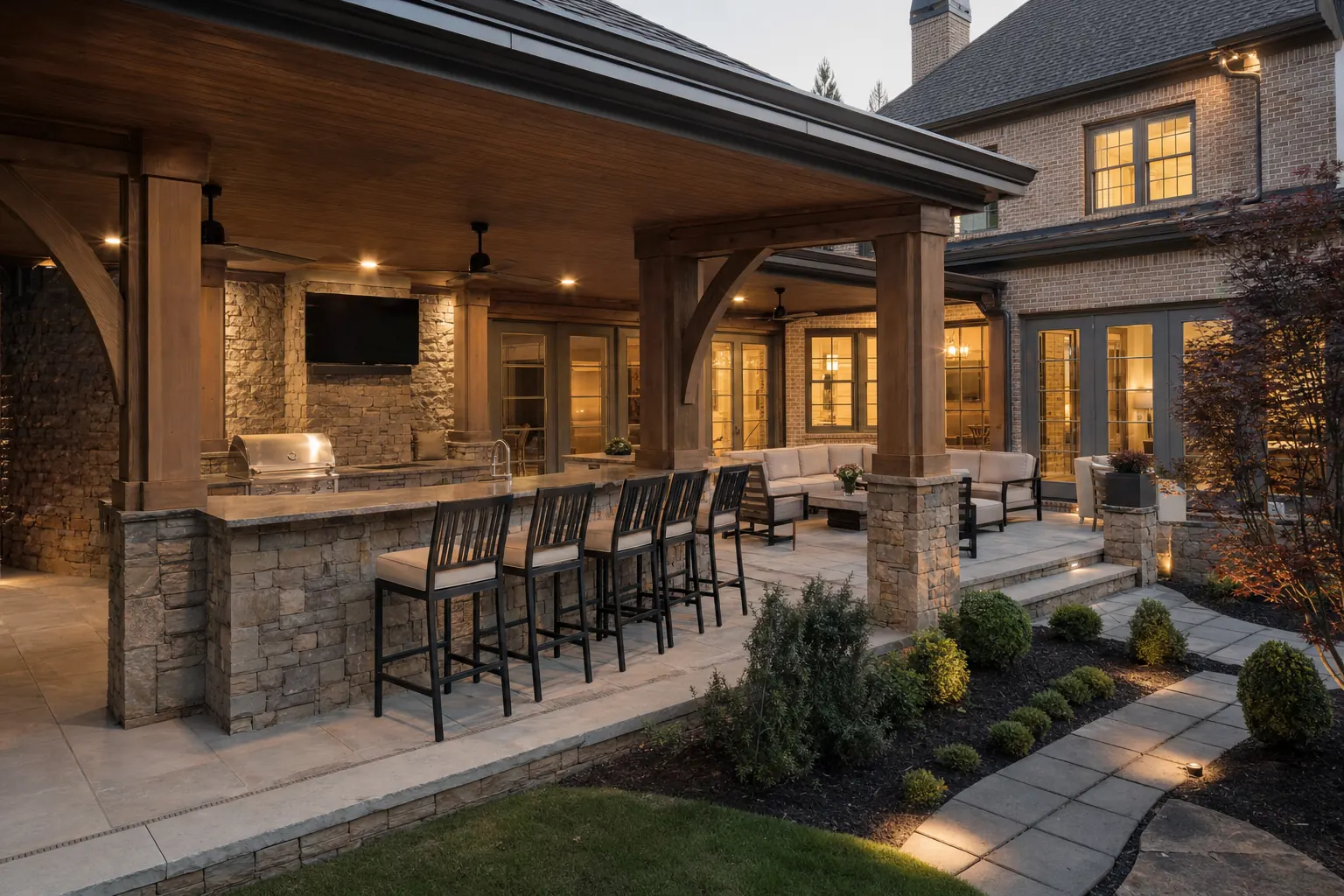 Covered patio with a stone outdoor kitchen, grill and bar seating behind a large brick home