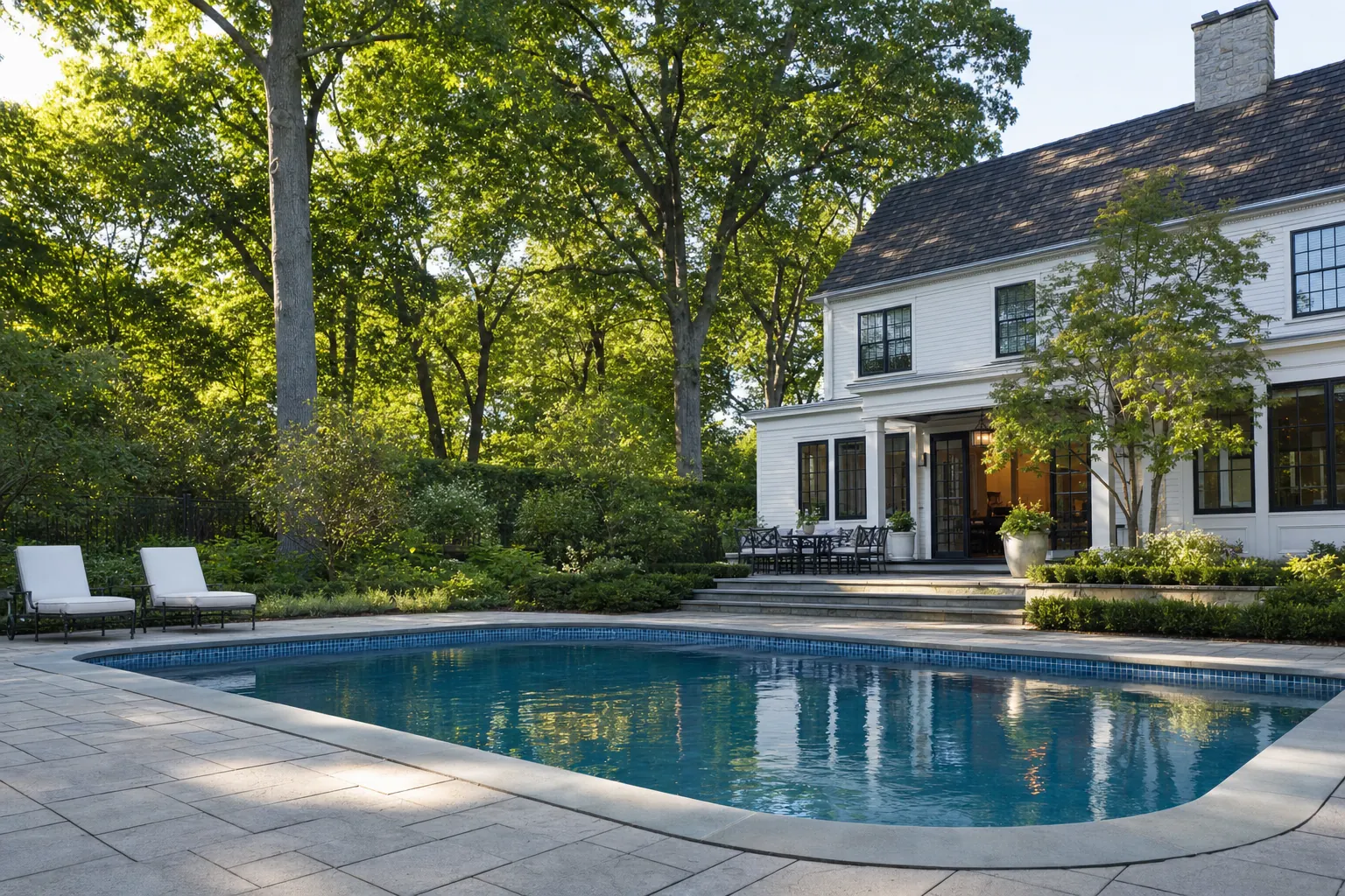 Older pool renovated with bluestone coping, a glass tile waterline and a new paver deck under tall hardwoods