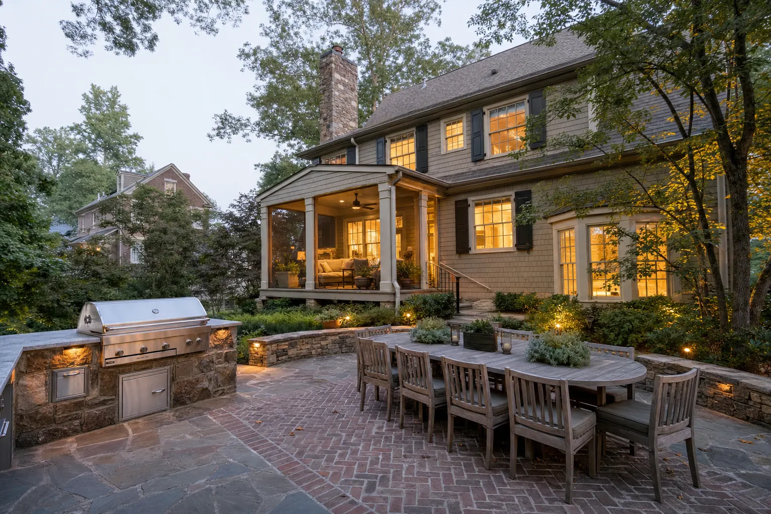 Brick and stone patio with an outdoor kitchen and dining table behind a two-story house