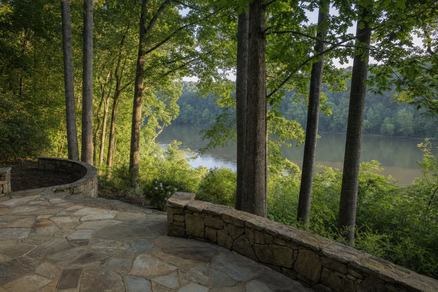 Flagstone terrace with a low stone wall at the top of a wooded slope above a wide river