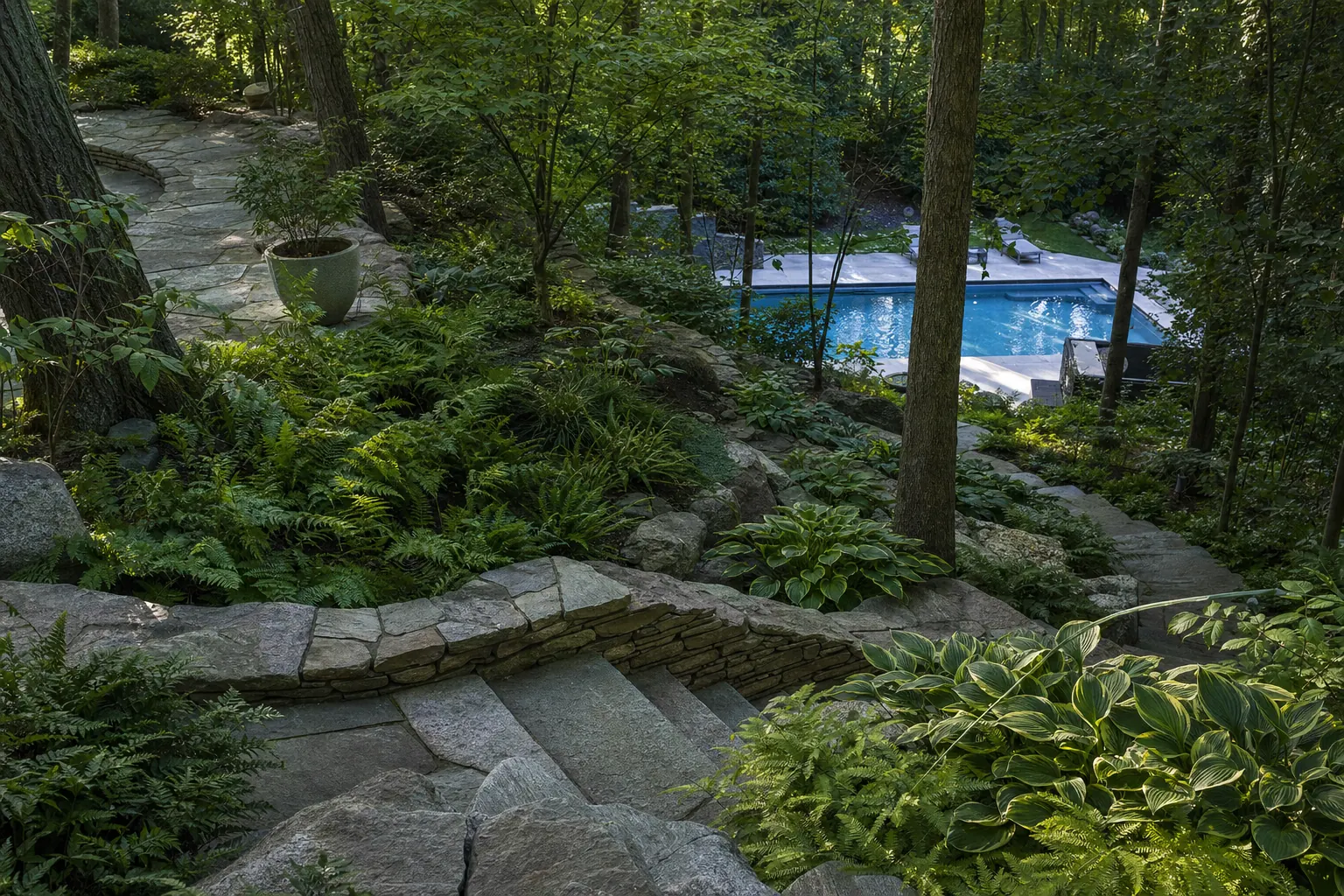 Stone stairs and terraces winding down a wooded slope to a pool deck